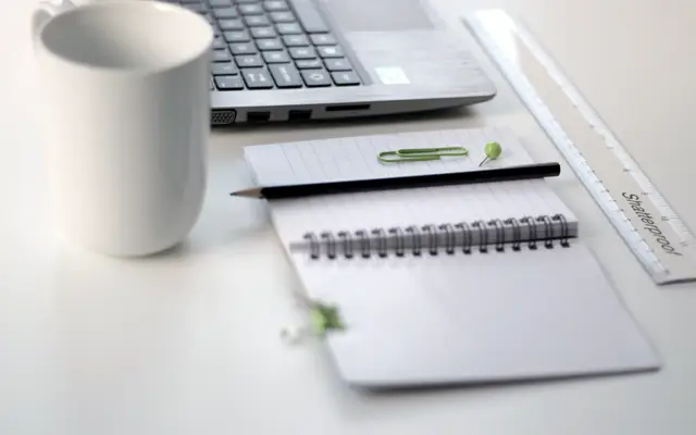 Notebook, pencil, coffee mug and laptop on a white desk