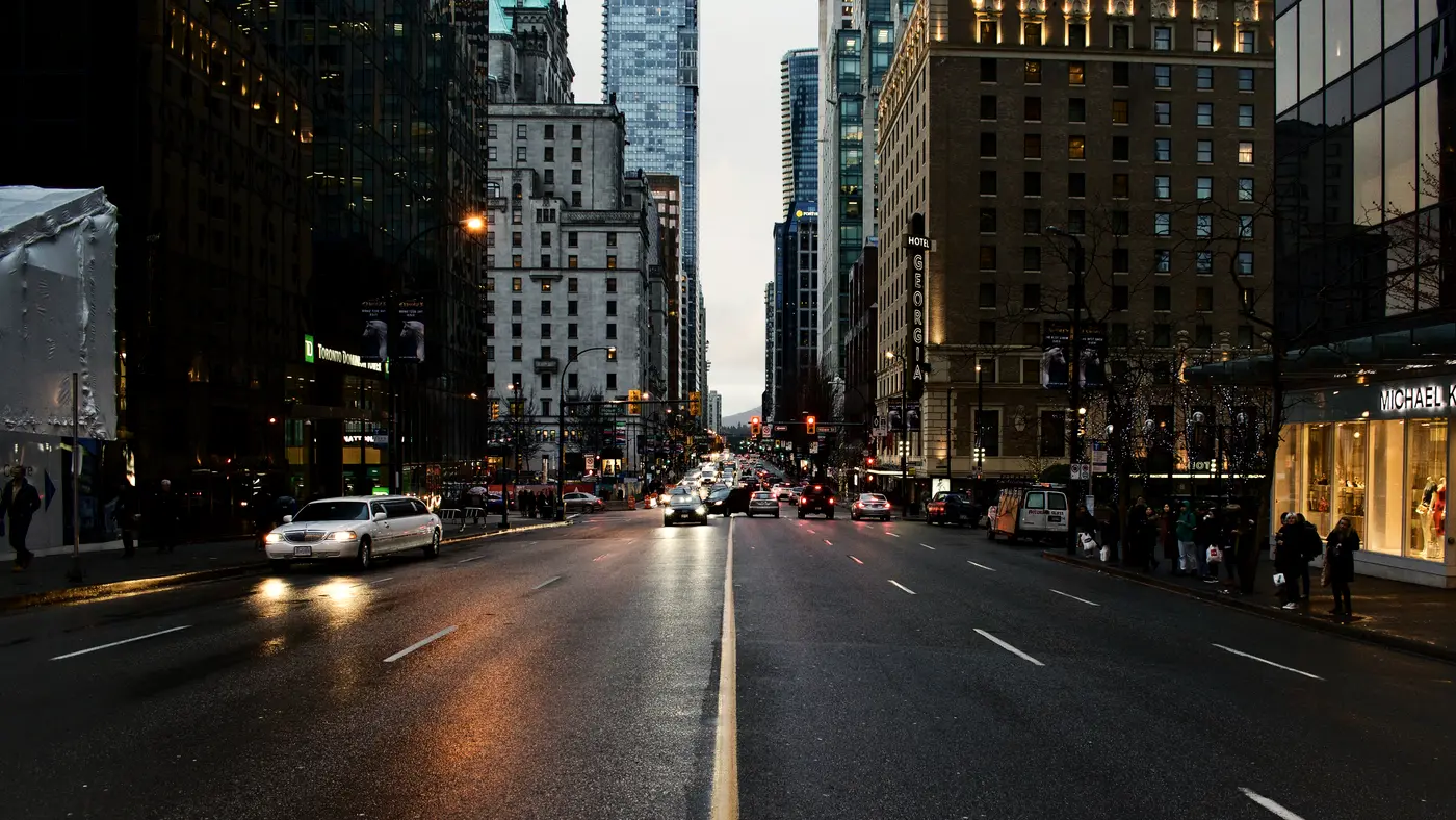 Wet downtown avenue at dusk lined with office towers