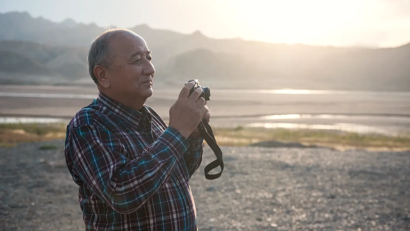 Older man holding a camera in soft evening light outdoors