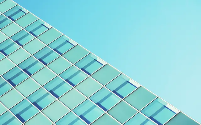 Blue glass office tower facade rising diagonally against clear sky