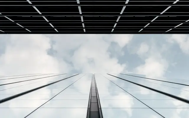 Looking up a glass skyscraper reflecting soft white clouds