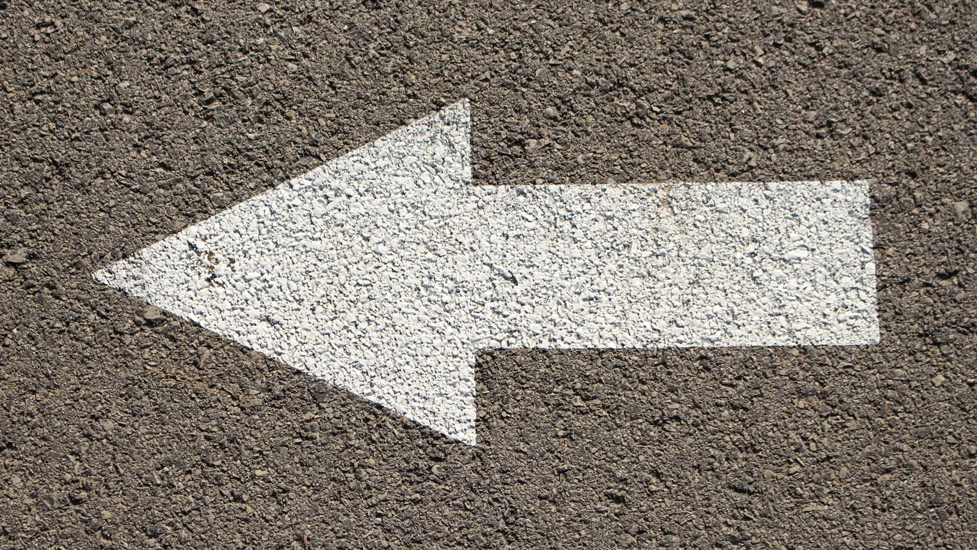 White arrow painted on dark asphalt pointing left
