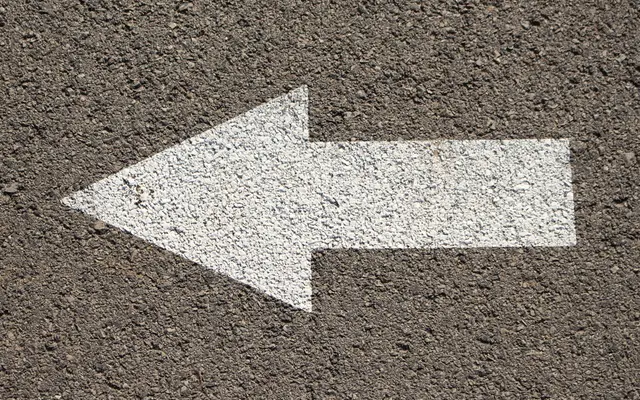 White arrow painted on dark asphalt pointing left